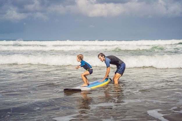 Père ou instructeur enseignant à son fils de 5 ans comment surfer dans la mer en vacances ou en vacances Concept de voyage et de sport avec enfants Leçon de surf pour les enfants