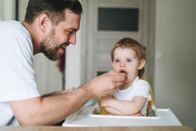 Père jeune homme nourrit petite fille petite fille dans la cuisine à la maison