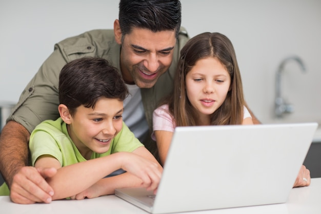 Père avec de jeunes enfants utilisant un ordinateur portable dans la cuisine