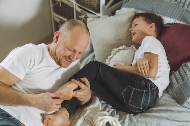 Père joue avec son fils 7-10 au lit. Papa chatouille les pieds des enfants. Famille, s'amuser