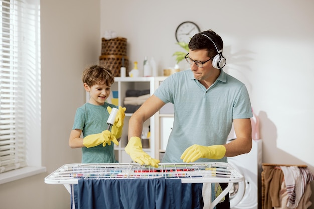 Un père joyeux passe du temps avec son fils dans la salle de bain de la buanderie, les hommes s'amusent pendant le nettoyage