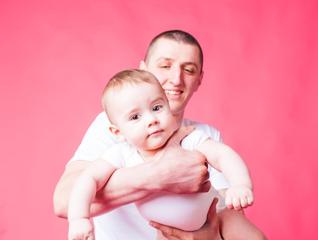 Le père joyeux tient les mains de son bébé bien-aimé sur fond rose