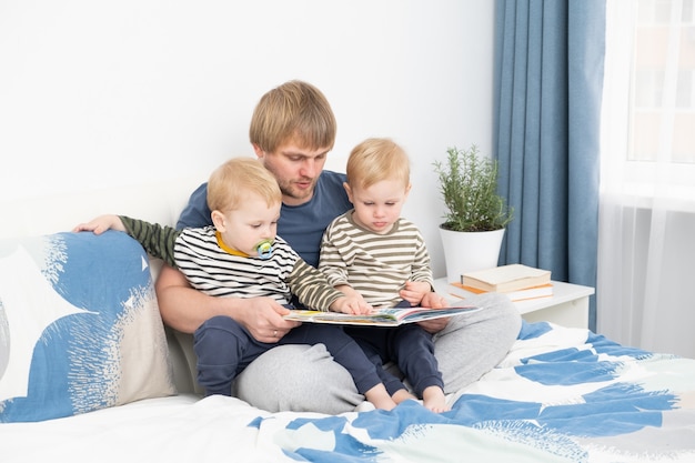 Père lisant un livre à ses fils jumeaux sur le lit à la maison passer du temps ensemble