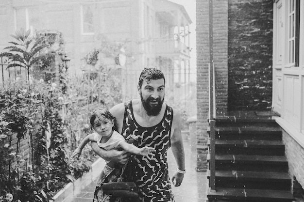 Photo père marchant avec sa petite fille à l'extérieur dans les rues de la vieille ville de tbilissi, dans la capitale de la géorgie, le jour de la pluie printanière papa fille s'enfuyant sous la pluie en ville photo touristique en noir et blanc