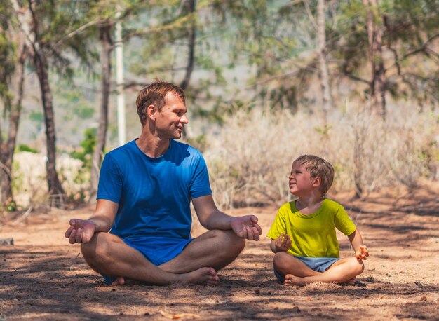 Photo le père médite la pose de yoga dans le parc forestier à l'air frais le fils répète un regard souriant et heureux l'influence de papa sur la vision du monde du garçon relation de paternité