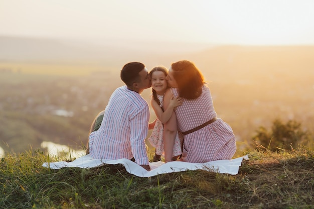 Père et mère embrassent la petite fille assise sur la colline