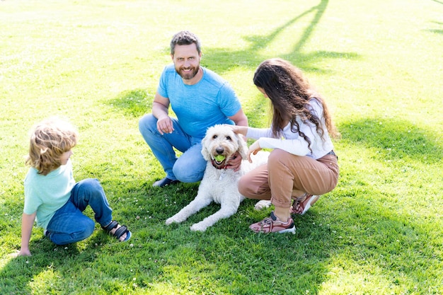 Père mère et enfant sur l'herbe verte du parc. famille sympathique avec animal de compagnie. parents heureux avec enfant garçon jouer avec chien. maman papa et fils adorent se détendre ensemble. l'adoption et la charité. journée familiale. relation amicale.