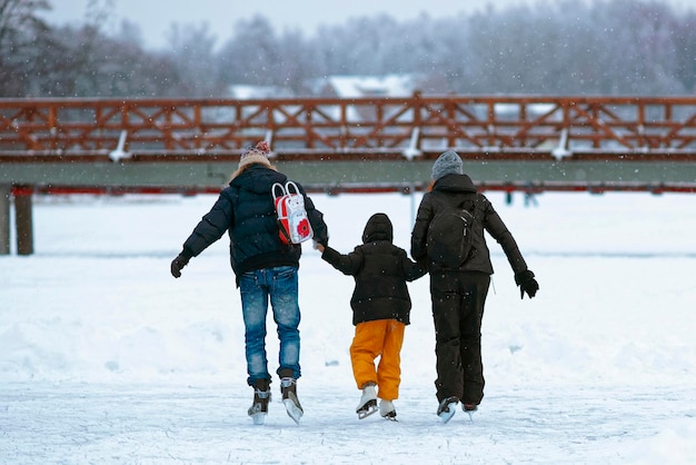 Père et mère enseignent à l'enfant à patiner sur la patinoire en hiver. Le patinage désigne toute activité sportive ou récréative qui consiste à se déplacer sur des surfaces ou sur la glace à l'aide de patins.