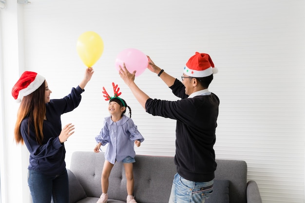 Père, mère et fille jouant aux ballons dans le salon. Ils sourient et sont heureux.