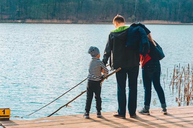 Père et mère avec garçon enfant jouant avec un banc près de l'eau