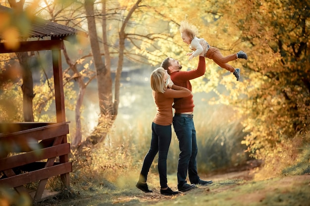 Père mère et petite fille dans les bras de leurs parents sur le chemin forestier entre les grands arbres jaunes