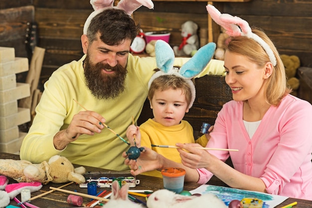 Père, mère et son enfant aiment peindre des œufs de Pâques.