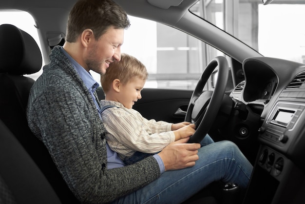 Père mignon avec fils assis sur le siège du conducteur dans une nouvelle voiture