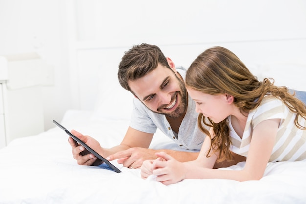 Père montrant une tablette numérique à sa fille sur le lit