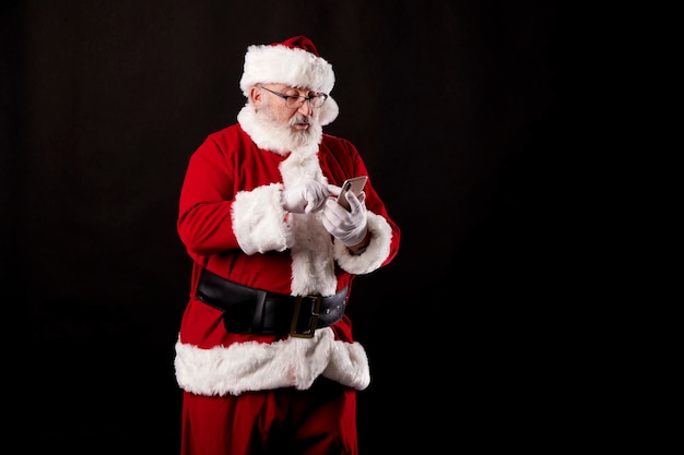 Père Noël à l'aide d'un téléphone mobile sur fond noir