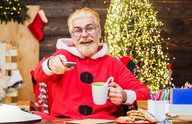 Le père noël assis dans un fauteuil regarde un film de noël et boit du café divertissement et cinéma