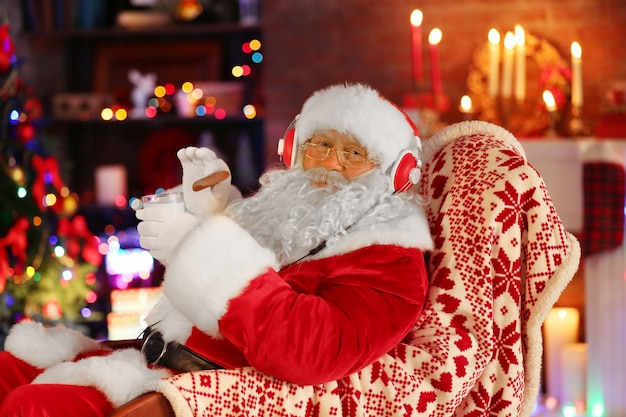 Père Noël assis avec des écouteurs assis dans une chaise berçante confortable à la maison
