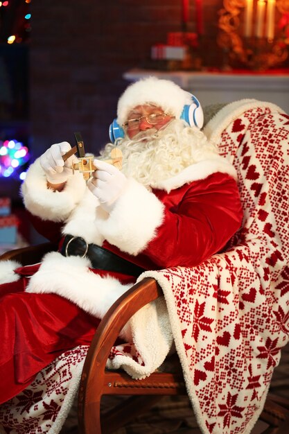 Père Noël assis avec des écouteurs assis dans un fauteuil à bascule confortable à la maison