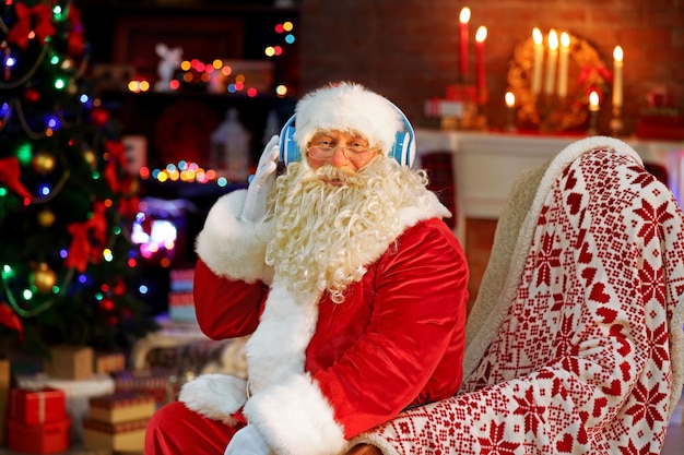 Père Noël assis avec des écouteurs assis dans un fauteuil à bascule confortable à la maison