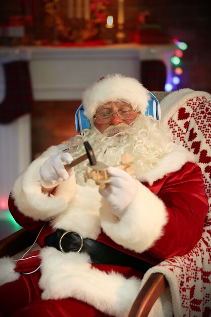 Père Noël assis avec des écouteurs assis dans un fauteuil à bascule confortable à la maison