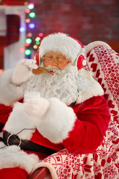 Père Noël assis avec des écouteurs assis dans un fauteuil à bascule confortable à la maison