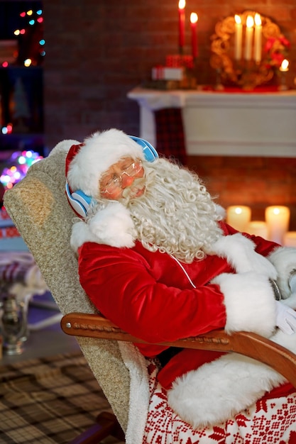 Père Noël assis avec des écouteurs assis dans un fauteuil à bascule confortable à la maison