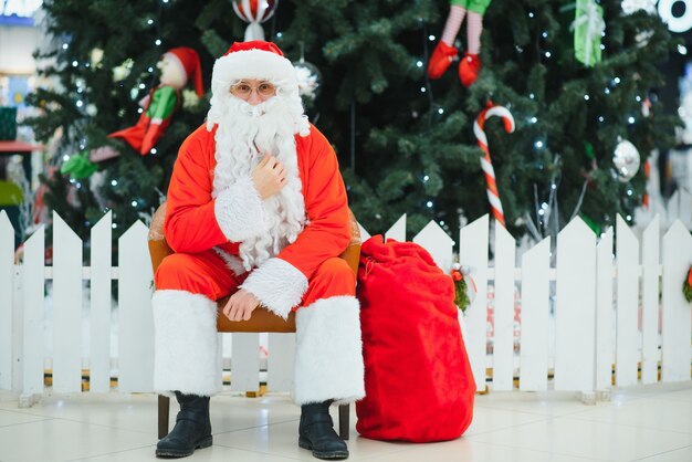 Père Noël assis sur le fond de l'arbre de Noël dans le hall du centre commercial moderne. Arrière-plan de base bokeh pour la conception.