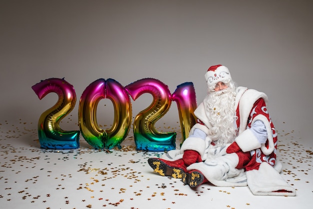 Père Noël assis sur le sol avec des ballons colorés en forme de 2021, photographie pour Noël et publicité du nouvel an