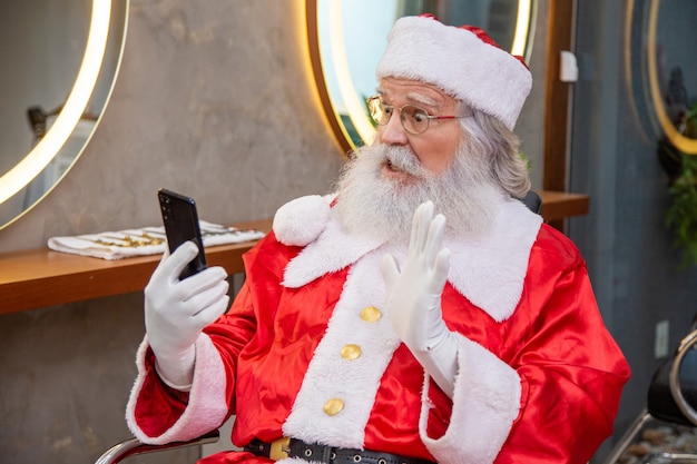 Le Père Noël au téléphone lors d'un appel vidéo tout en se préparant dans le salon de beauté pour le réveillon de Noël