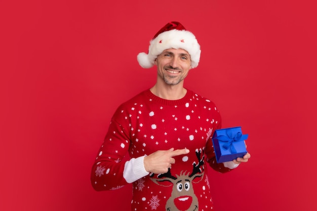 Père Noël avec boîte-cadeau Homme en pull de vacances et bonnet de Noel sur fond de studio Vente de Noël ou offre spéciale d'hiver