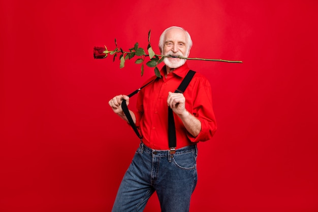 Père Noël en bretelles et chapeau posant sur un mur rouge