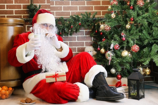 Père Noël avec des cadeaux assis à côté d'un arbre de Noël