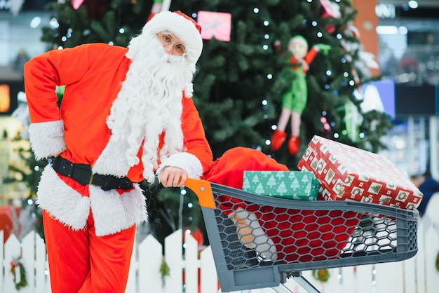 Père Noël avec des cadeaux dans le centre commercial sur le fond de l'arbre de Noël