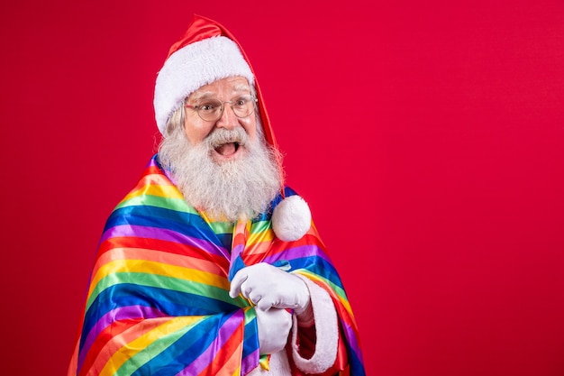 Père Noël couvrant avec le drapeau de la fierté LGBT. Tout seul. Une. Gardez le poing levé, couvrant le drapeau LGBT. Drapeau LGBT + sur fond rouge. Noël.