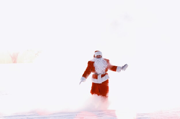 Père Noël dans le domaine de l'hiver. Brouillard magique de Santa marchant le long du champ. Le Père Noël la veille de Noël porte des cadeaux aux enfants dans un sac rouge