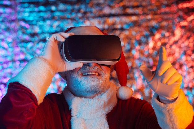 Père Noël dans des lunettes VR faisant des gestes, il joue au jeu vidéo