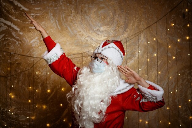 Le père noël dans des verres et un masque montre des gestes avec ses mains sur le fond d'un mur avec un g...