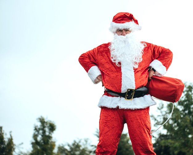Père Noël debout avec les bras reposant sur ses hanches saisissant son sac rouge. période de Noël