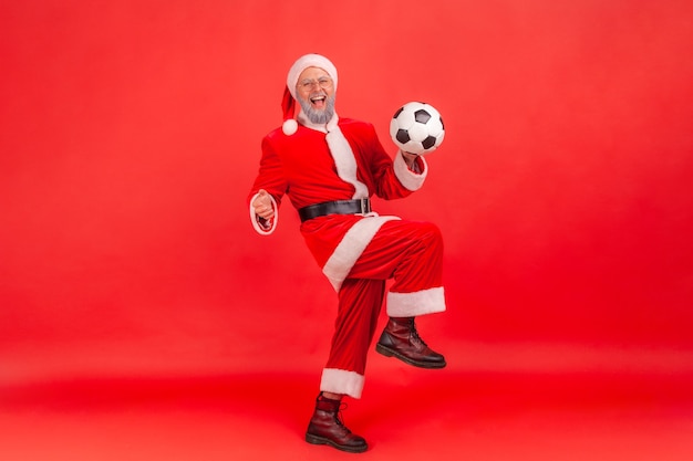 Père Noël debout et jouant avec un ballon de football, célébrant l'équipe favorite gagnante.