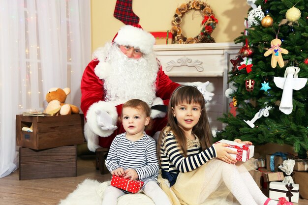 Père Noël avec deux petites filles mignonnes près de la cheminée et de l'arbre de Noël à la maison