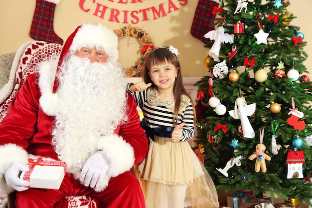 Père Noël donnant un cadeau à une petite fille mignonne endormie, un arbre de Noël à la maison