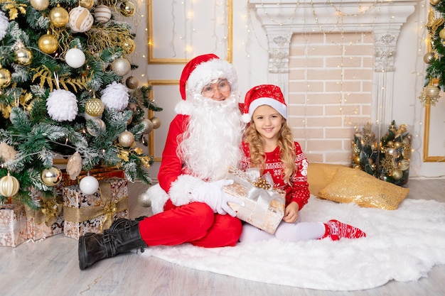 Le Père Noël donne un cadeau à une petite fille à l'arbre de Noël