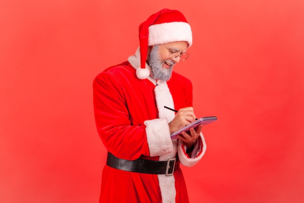 Le père noël écrit dans un cahier, fait une liste de souhaits pour les vacances de Noël.