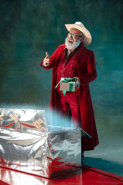 Père Noël élégant et moderne en costume à la mode rouge et chapeau de cowboy sur fond sombre