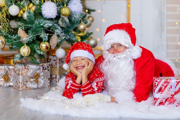 Père Noël avec un enfant près de l'arbre de Noël étreignant