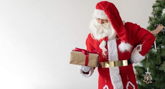 Le Père Noël est debout près de l'arbre de Noël, tenant une boîte avec un cadeau et le regardant.