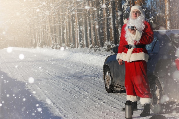 Le Père Noël est livré avec des cadeaux de l'extérieur. Le Père Noël en costume rouge avec une barbe et portant des lunettes marche le long de la route de Noël. Le Père Noël apporte des cadeaux aux enfants.