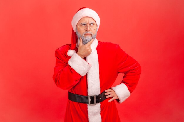 Père noël avec une expression pensive, tenant le menton, pensant aux futures vacances.