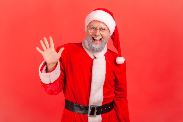 Le père noël levant la paume pour saluer, saluant avec un sourire amical et hospitalier.