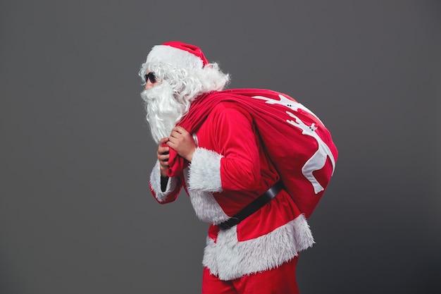 Le Père Noël avec des lunettes de soleil court avec le sac de cadeaux de Noël sur le dos sur fond blanc. .